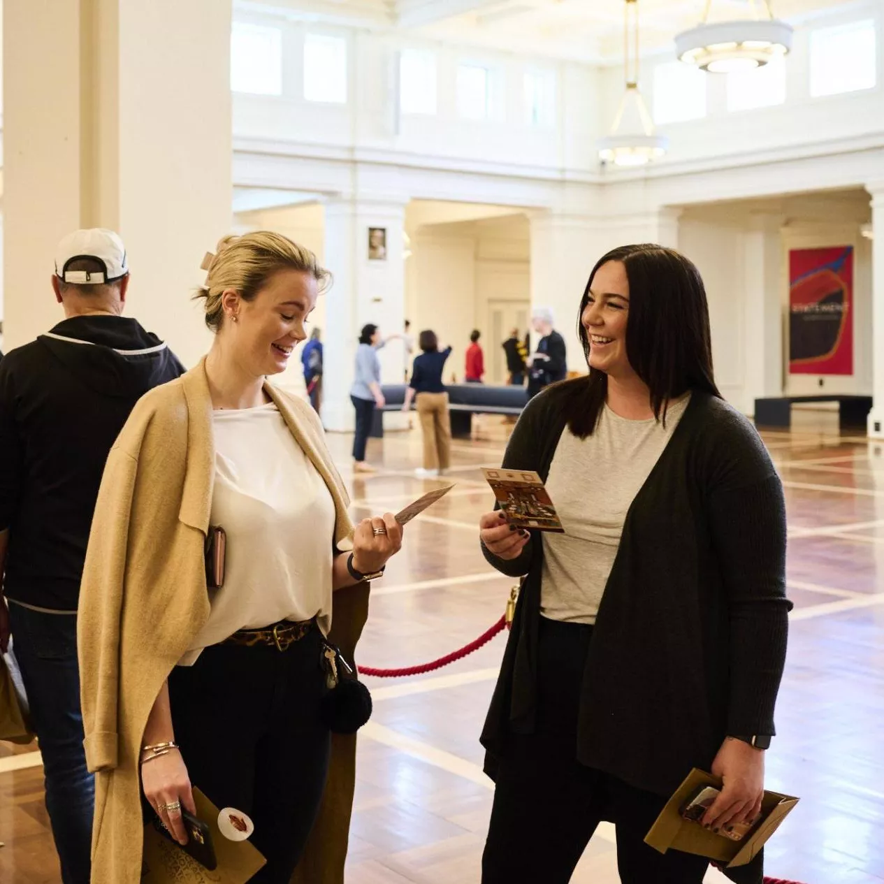 Two women talk to each other in a queue in King's Hall. 