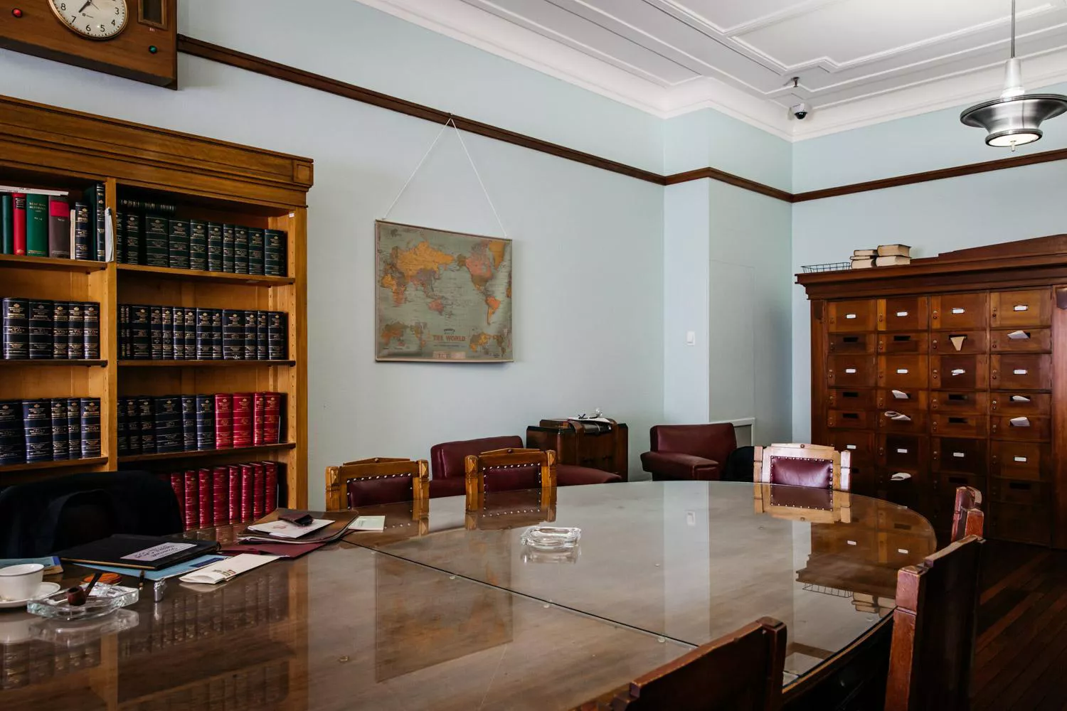 A modern-day view of the Country Party Room. A large, varnished wooden table with a rounded end takes up the majority of the room, with chairs around it. There is a wooden bookcase on the wall to the back, then a unit of drawers against the wall at the end.