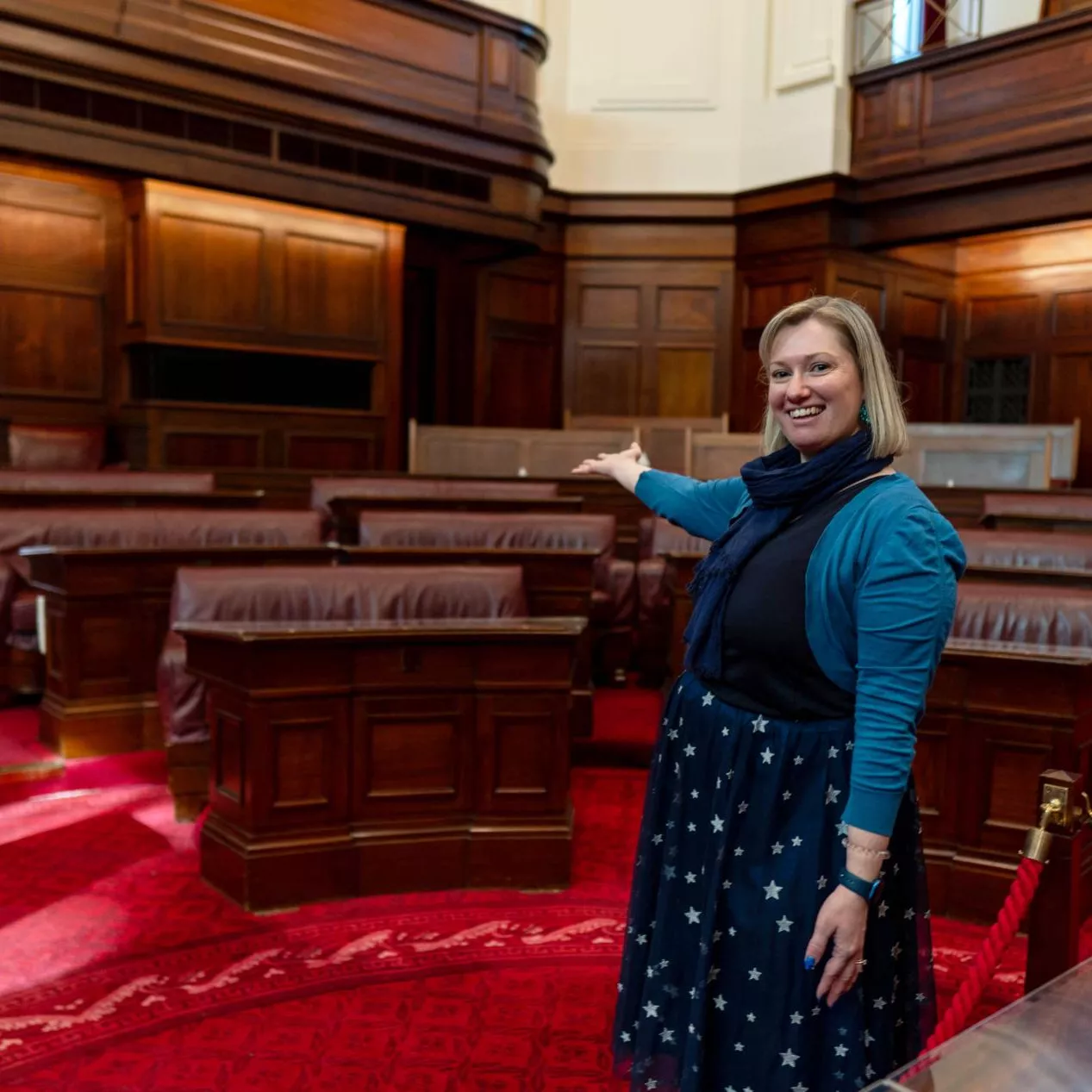 A person stands with their arm outstreched in the senate chamber at old parliament house