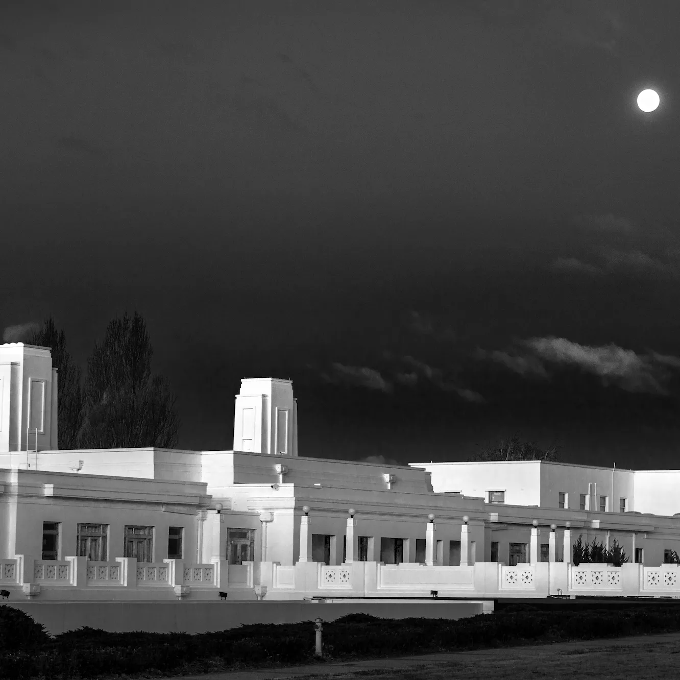 A long white building, Old Parliament House, with a dark sky and the moon in the background.