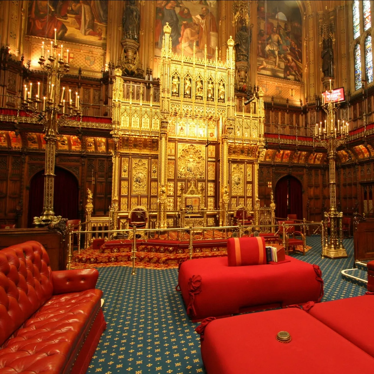 The House of Lords at Westminster, with a golden throne, red leather benches on each side, and big red cushions in the middle.