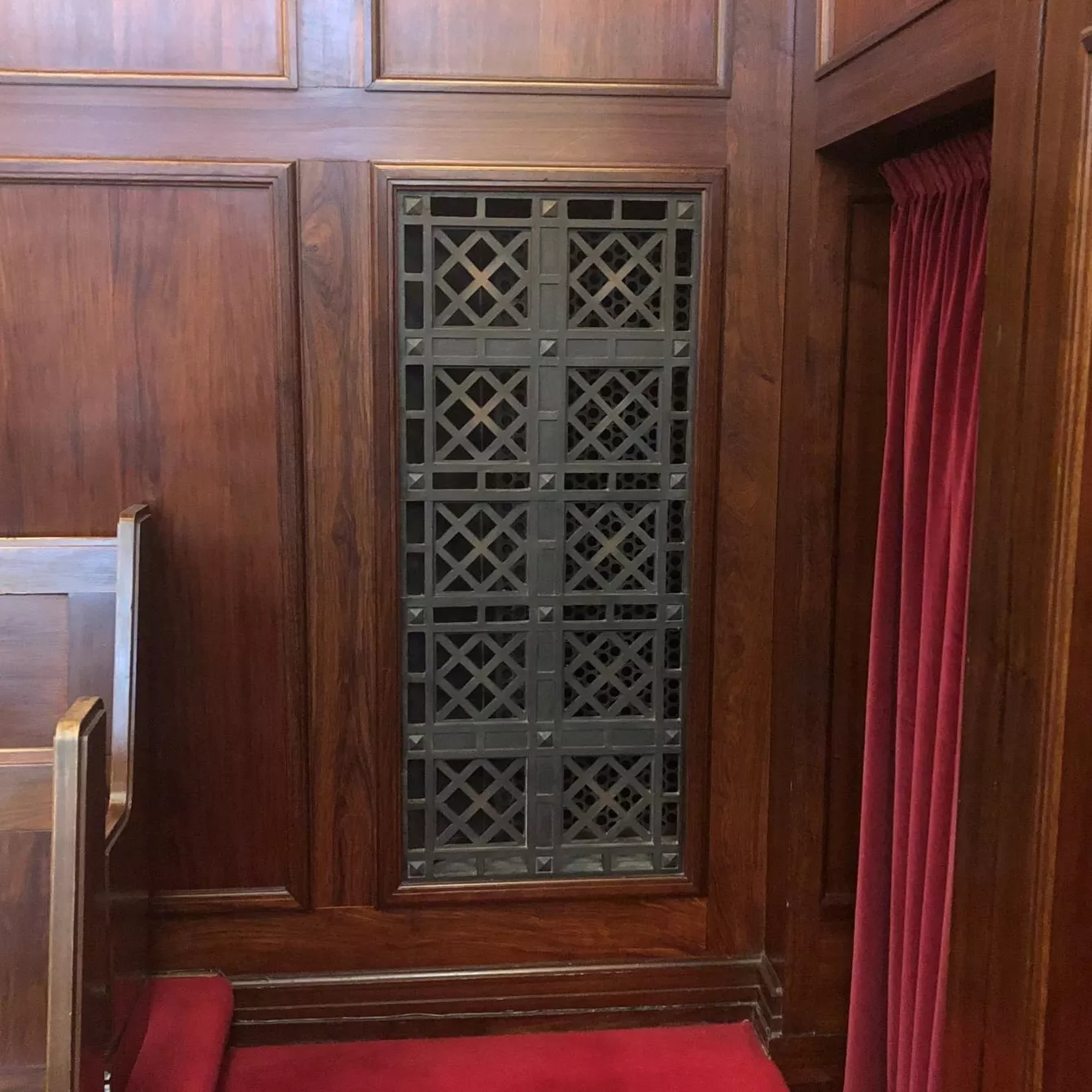 Rectangular bronze vent cover with a diagonal square pattern, inset in a wooden panelled wall.