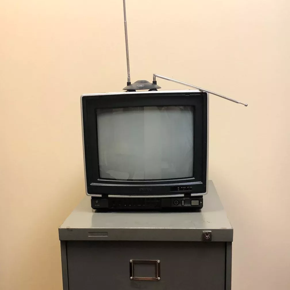 A small television with an aerial antenna sits on top of a grey filing cabinet.