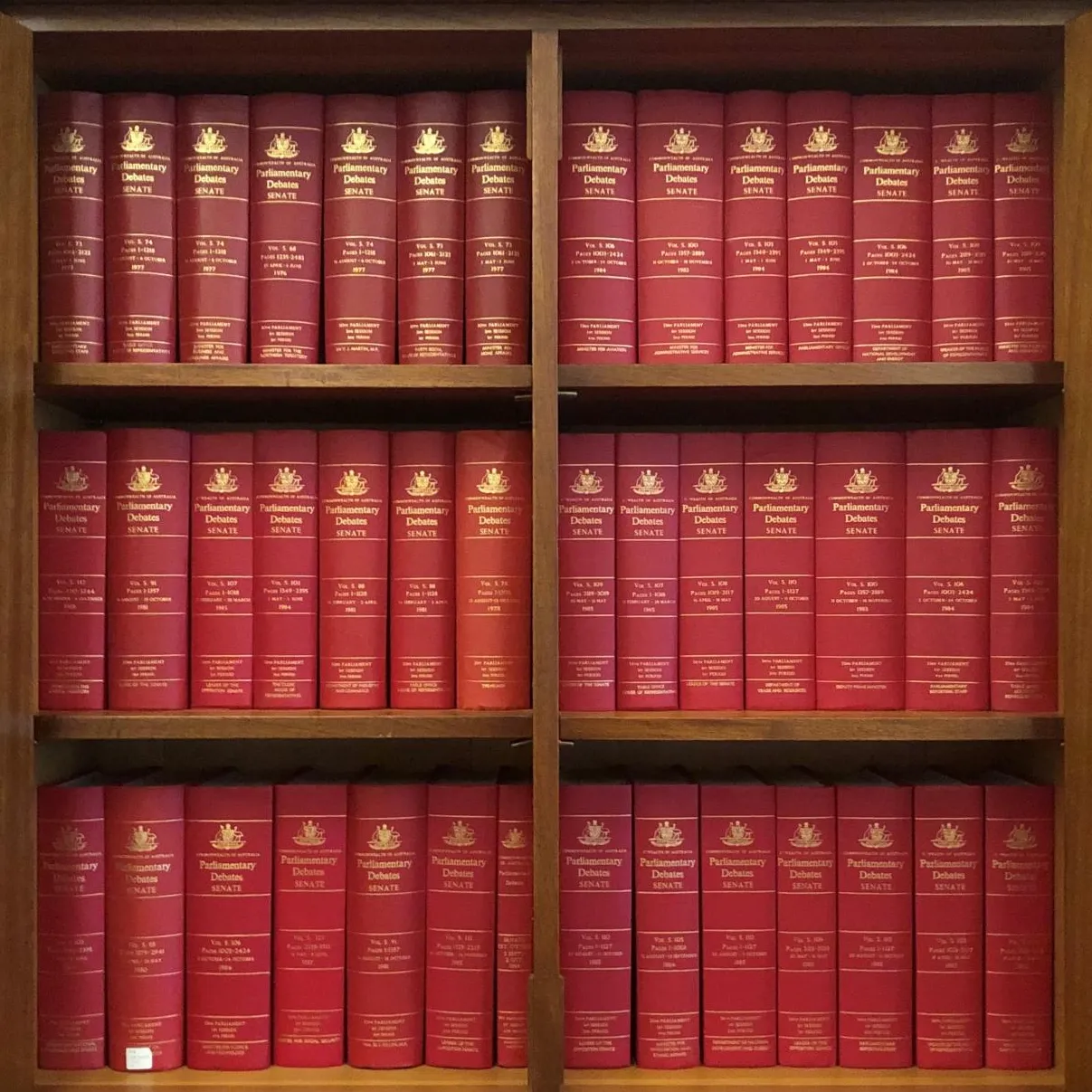 A wooden shelf with opened glass doors holds three rows of red bound volumes labelled 'Parliamentary Debates; Senate' on the spines.