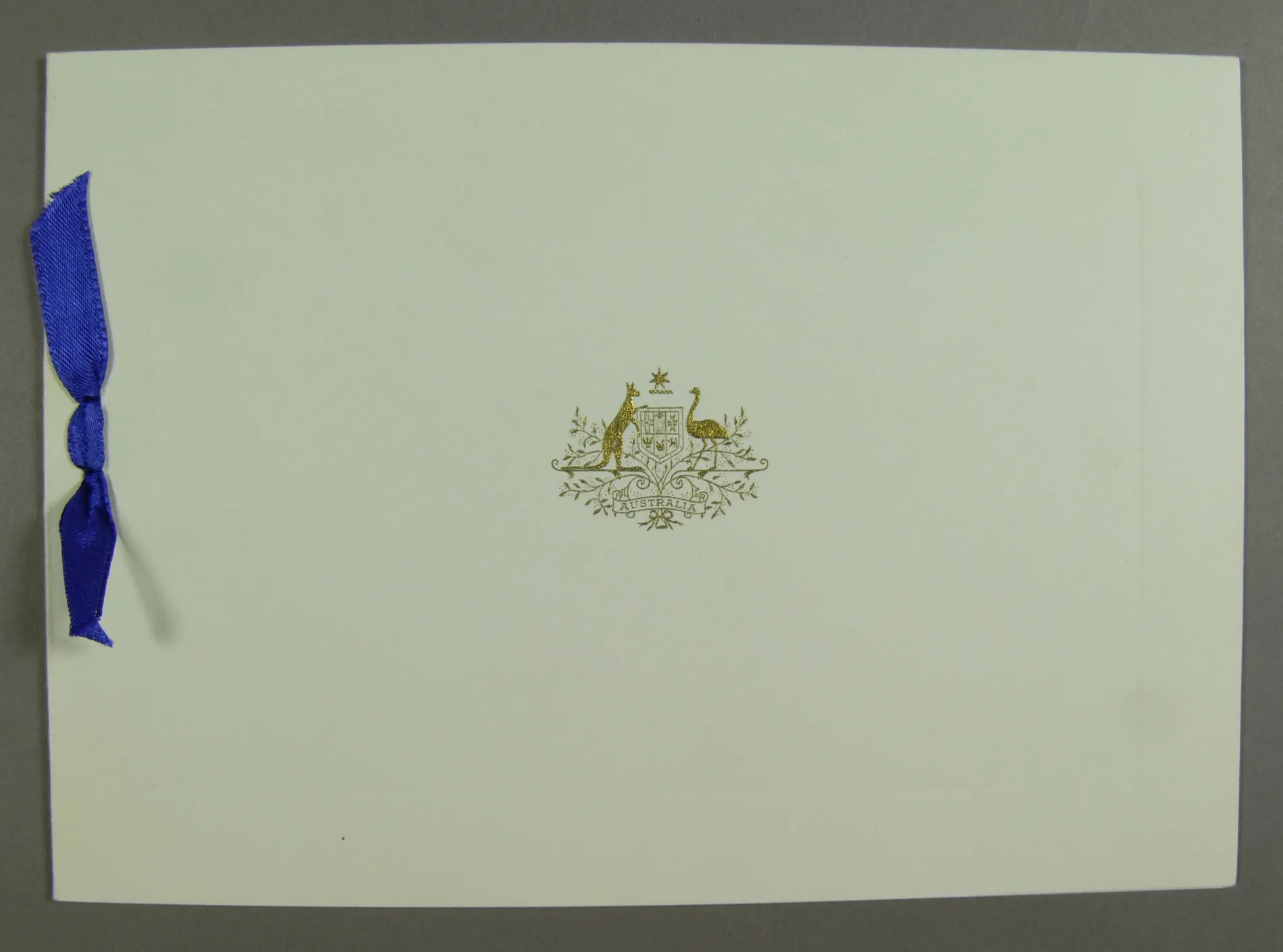 A white card cover, embossed in gold with the Australian coat of arms and bound with a blue ribbon.