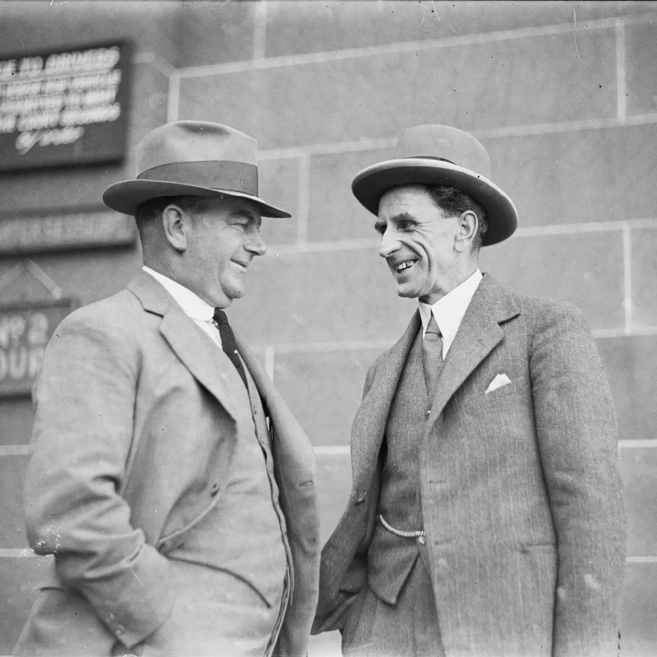 Donald Grant (on the right) smiling and speaking with another man, both wearing wide-brimmed hats and three-piece suits.