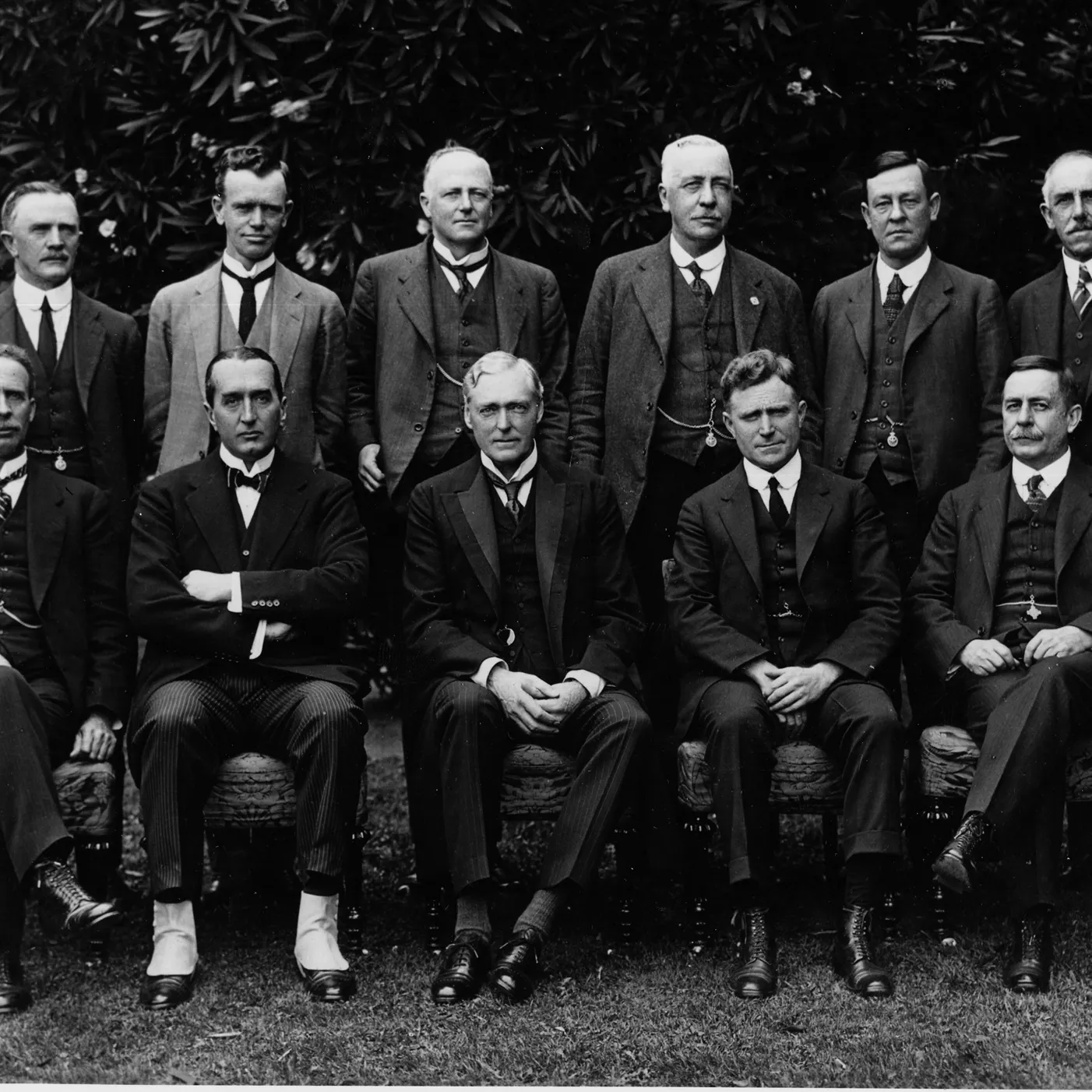 Black and white photograph of eleven men, posing in two rows, all wearing three-piece suits.