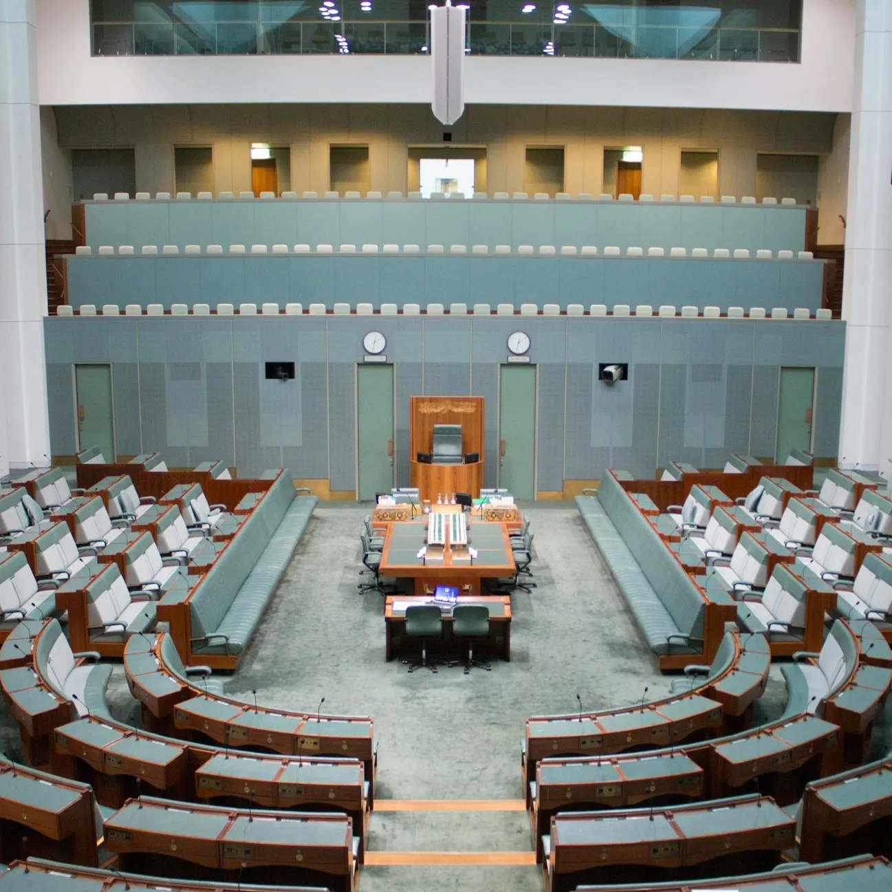 The House of Representatives, a room with grey-green furnishings, with benches arranged in a horse-shoe shape around a central long bench and chair.