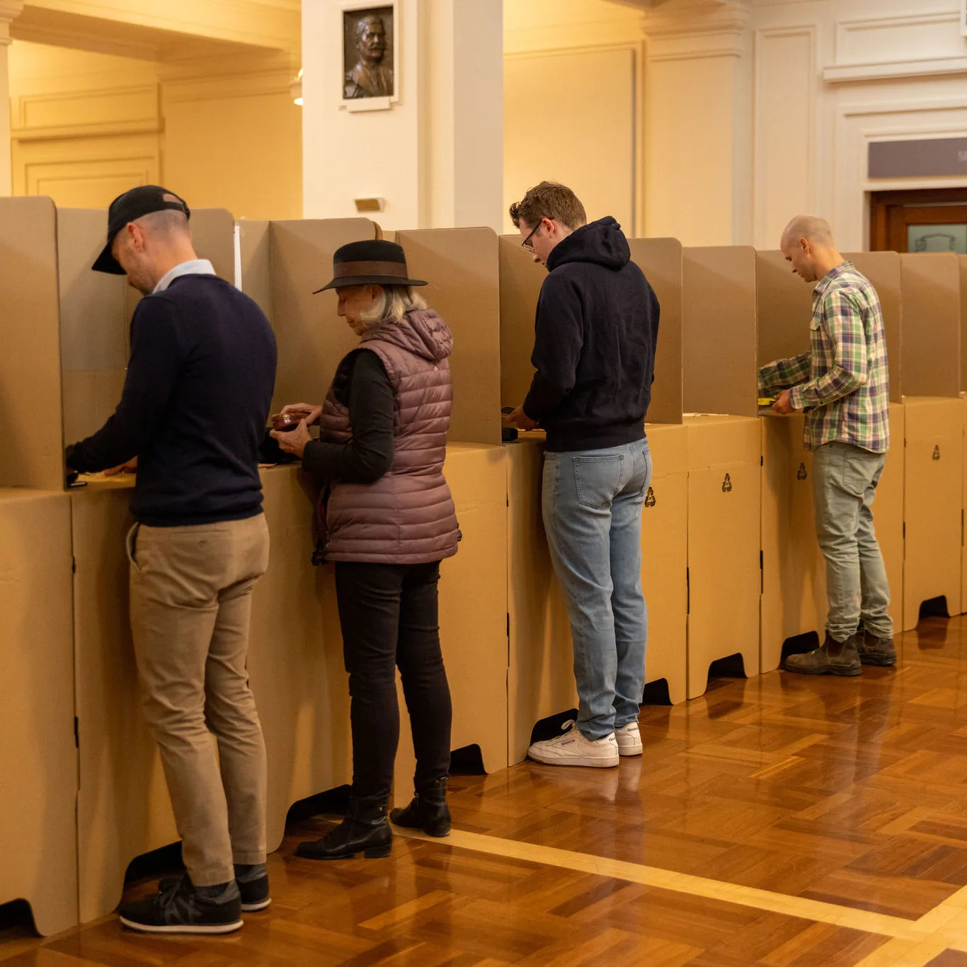 Four people, three men and a woman, standing at cardboard election booths in King's Hall.