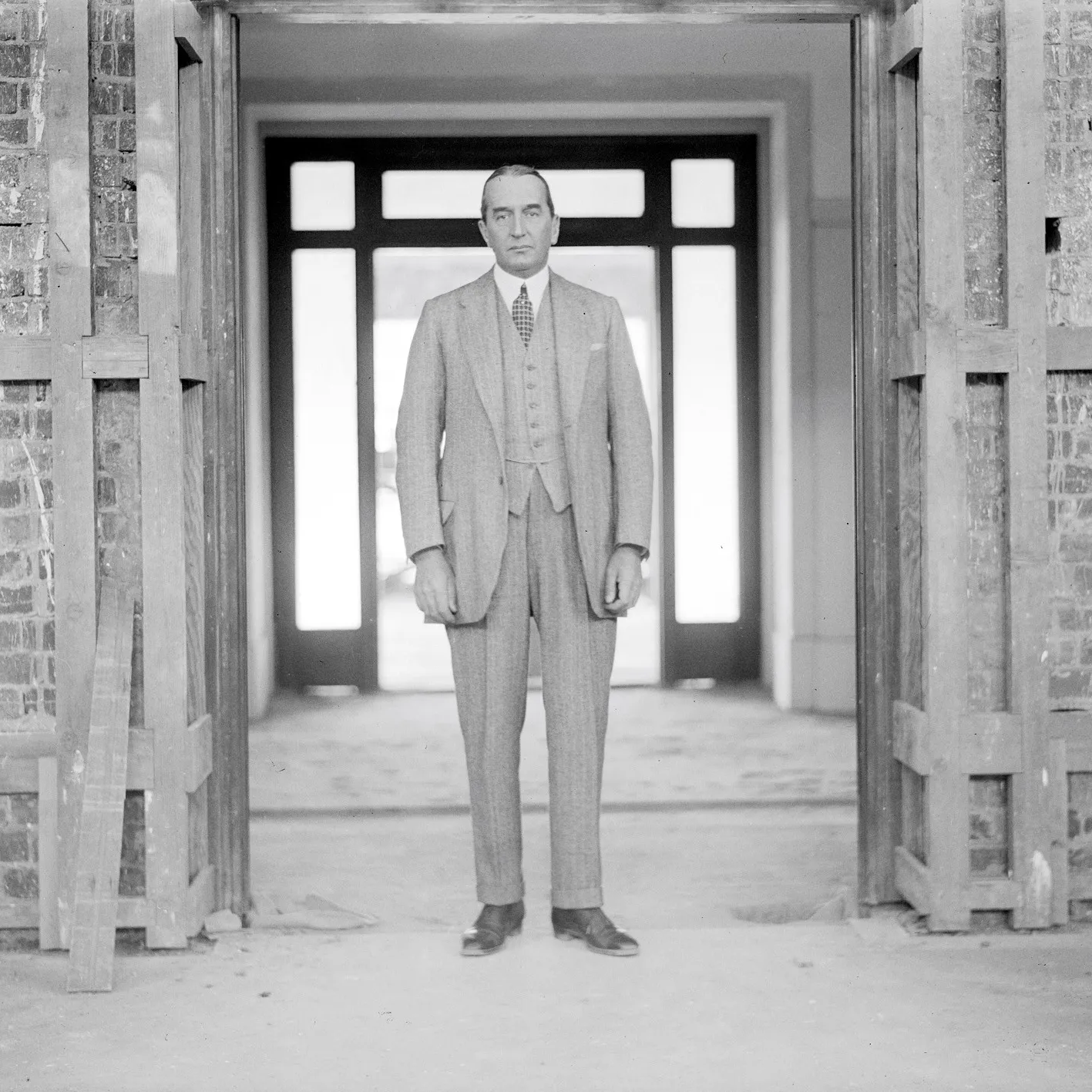 Black and white photograph of Stanley Bruce, wearing a three-piece suit, standing in a doorway at the construction site of Old Parliament House.