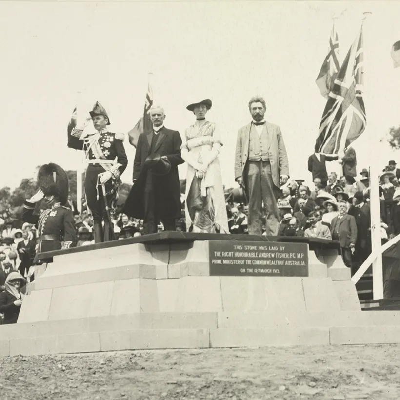 Governor-General Denman, Prime Minister Fisher, Lady Denman and King O'Malley stand on a commemorative stone. British and Australian flags are the in background, with a large crowd behind.