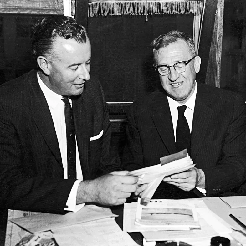 Arthur Calwell and Gough Whitlam are both holding and looking at some papers.