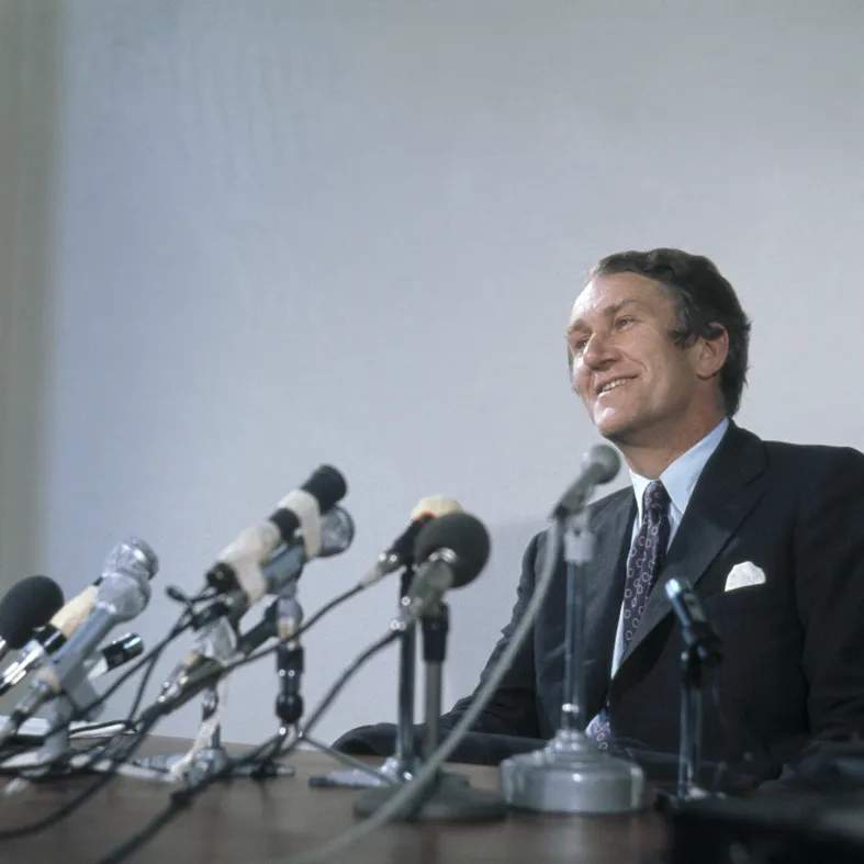 Malcolm Fraser looks out from behind a desk with microphones on it.