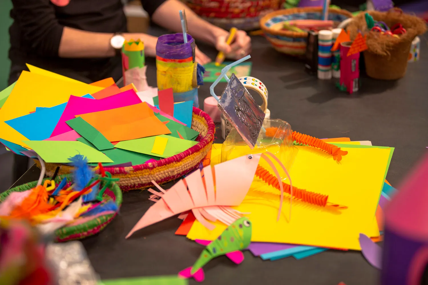 A black-covered table filled with coloured paper and crafting supplies.