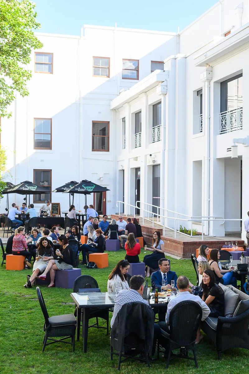 People sit and have drinks in the sunny courtyard of Old Parliament House.