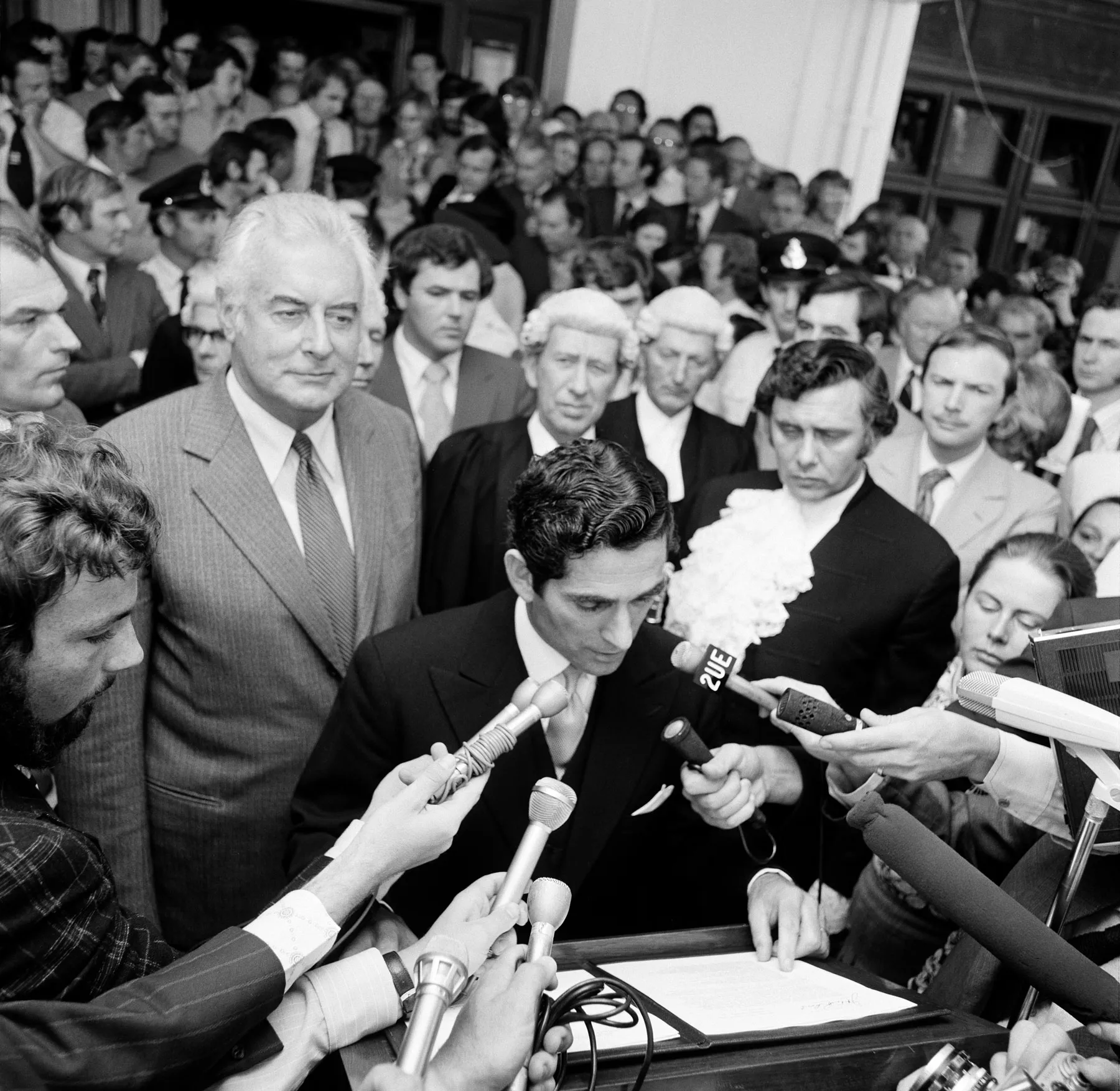 David Smith reads the dismissal outside Old Parliament House while Gough Whitlam stands by his side. The press and a big crowd surround them.