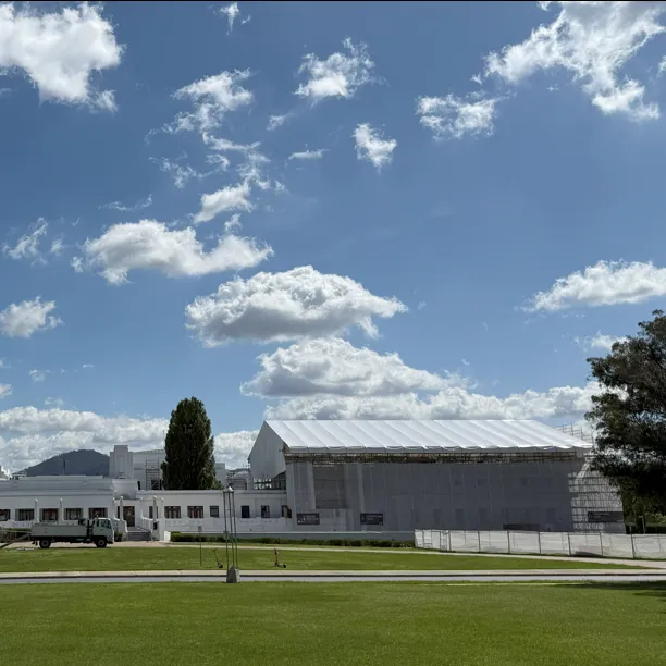 A view of the back of Old Parliament House, a long white building with a white scaffolding over one section of the roof and walls. 