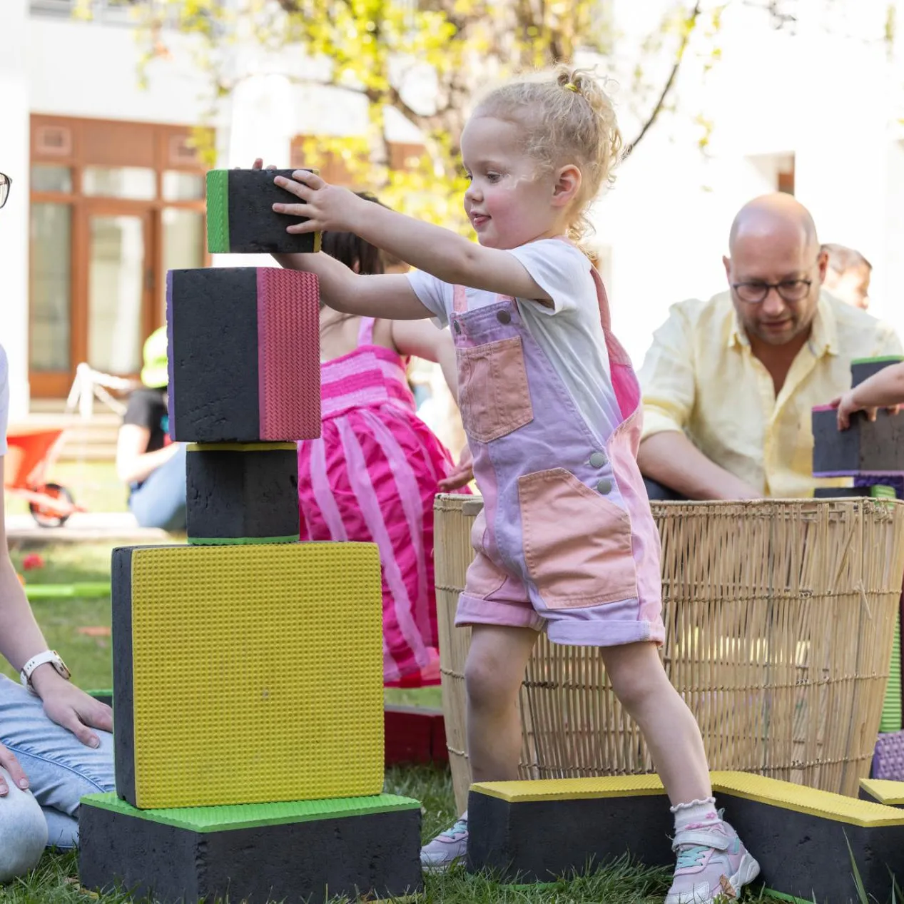 Kids and their parents play with large colourful blocks on the grass of the Old Parliament House courtyard.