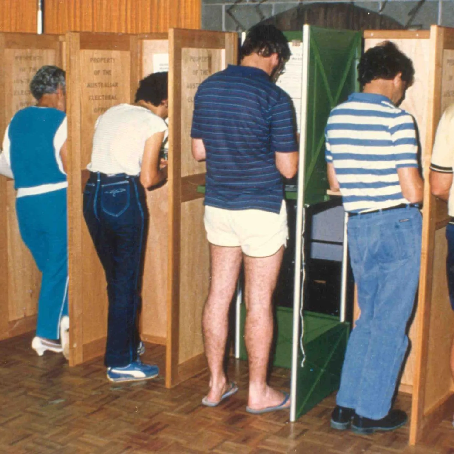 Men and women dressed in 1970s fashion vote in partitioned booths which are labelled 'Property of the Australian Electoral Office'.