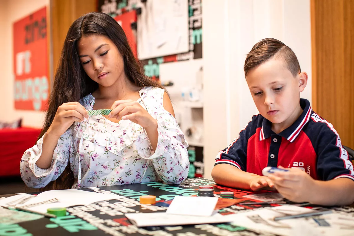 A boy and a girl sit at a table with craft supplies using sticky tape and drawing.