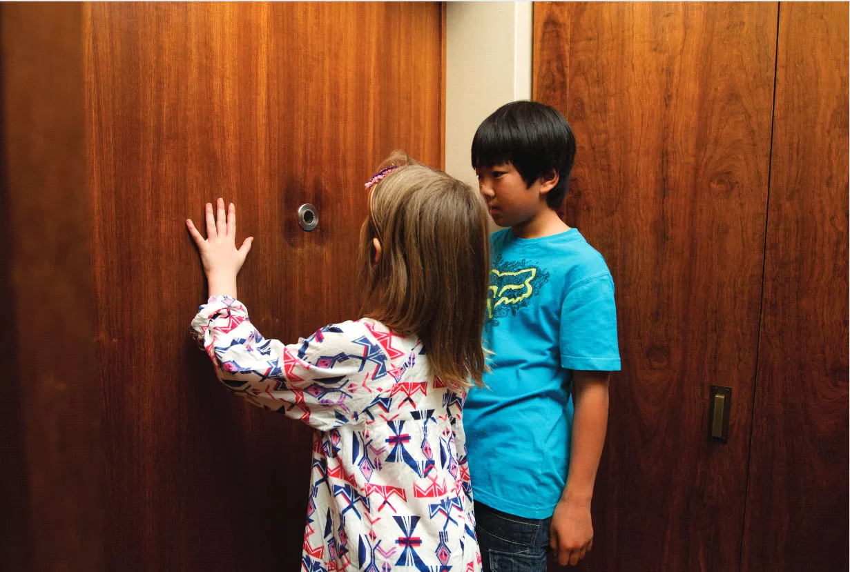 Two children investigating what appears to be a spy-hole in a wooden wall Two children investigating what appears to be a spy-hole in a wooden wall