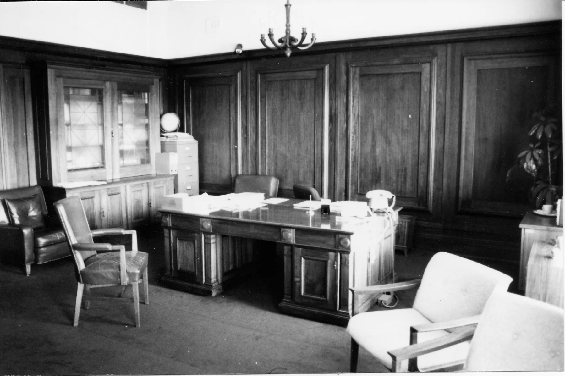 This black and white photograph shows the layout of the Clerk of the Senate’s office in 1985 when it was occupied by Alan Cumming Thom. The timber-panelled room contains a large desk (originally designed by the building’s architect, John Smith Murdoch), glass-fronted built-in bookshelves and a sideboard with an indoor plant. There are a range of visitor chairs and an easy chair in the foreground. This black and white photograph shows the layout of the Clerk of the Senate’s office in 1985 when it was occupied by Alan Cumming Thom. The timber-panelled room contains a large desk (originally designed by the building’s architect, John Smith Murdoch), glass-fronted built-in bookshelves and a sideboard with an indoor plant. There are a range of visitor chairs and an easy chair in the foreground.