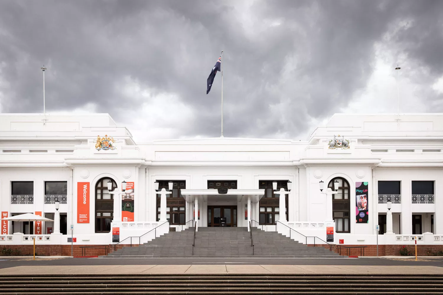 A large staircase leads up to a white old building with a flag on the top.