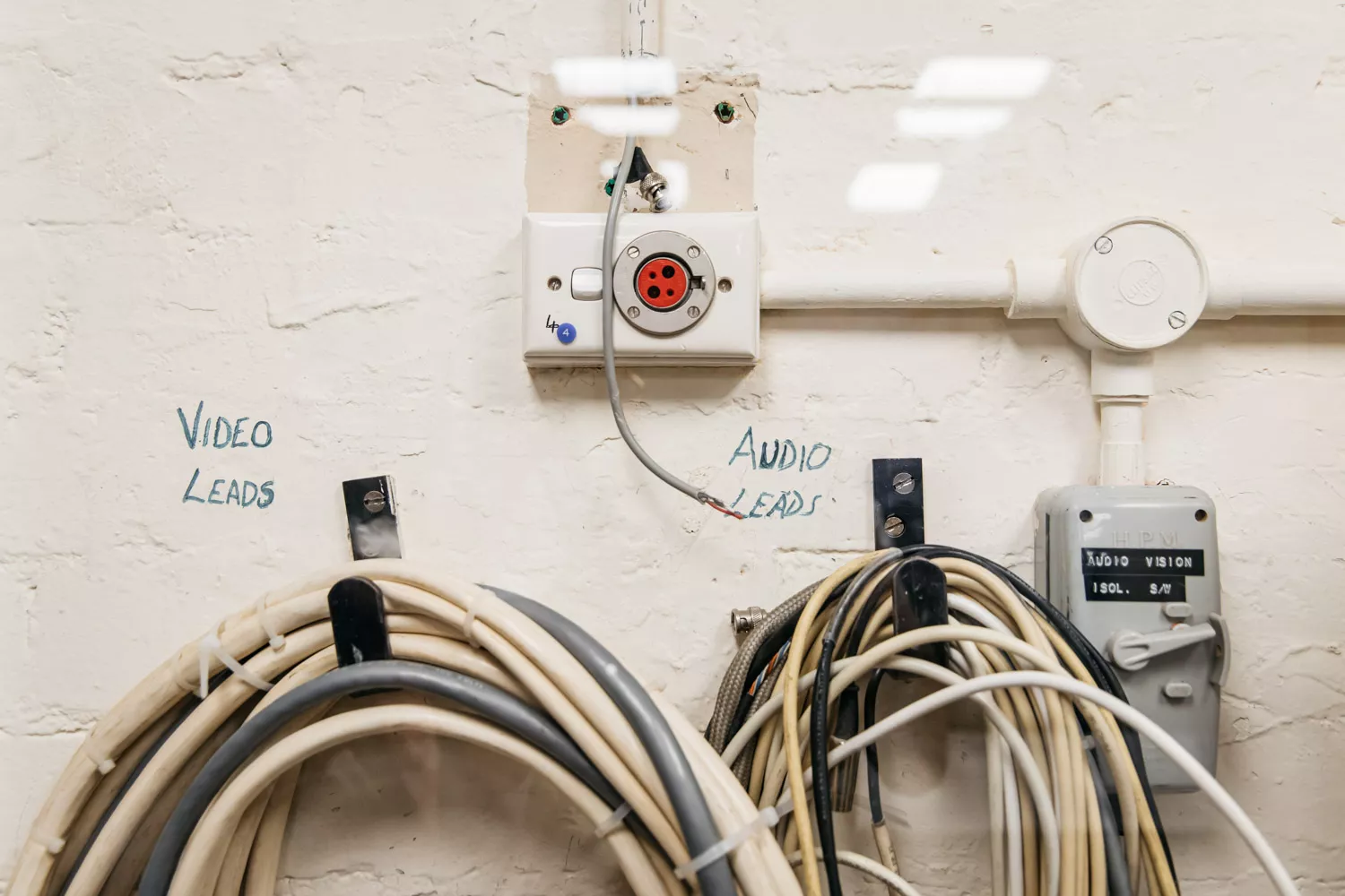 Piles of phone cables in loops hung on a wall with the words video leads and audio leads above them in texta. 