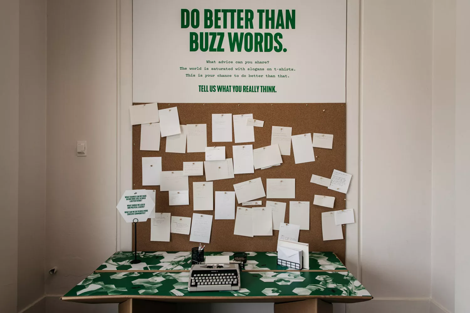 A pinboard with lots of notes and a typewriter in front of it and a sign that reads 'do better than buzzwords'.