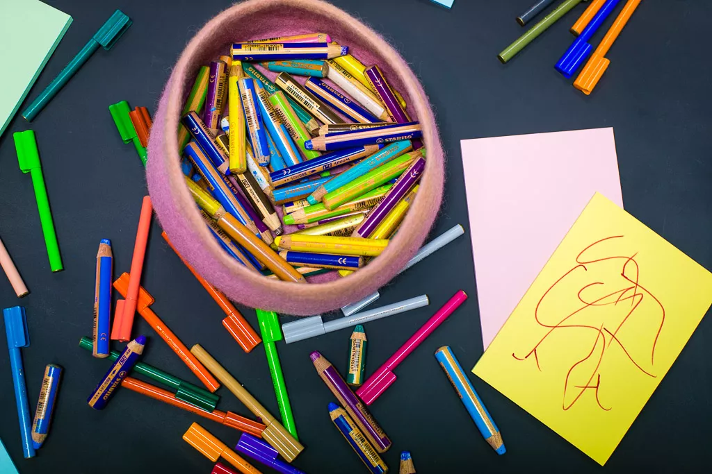 A close up of a circular felt container of pens, textas and crayons. 