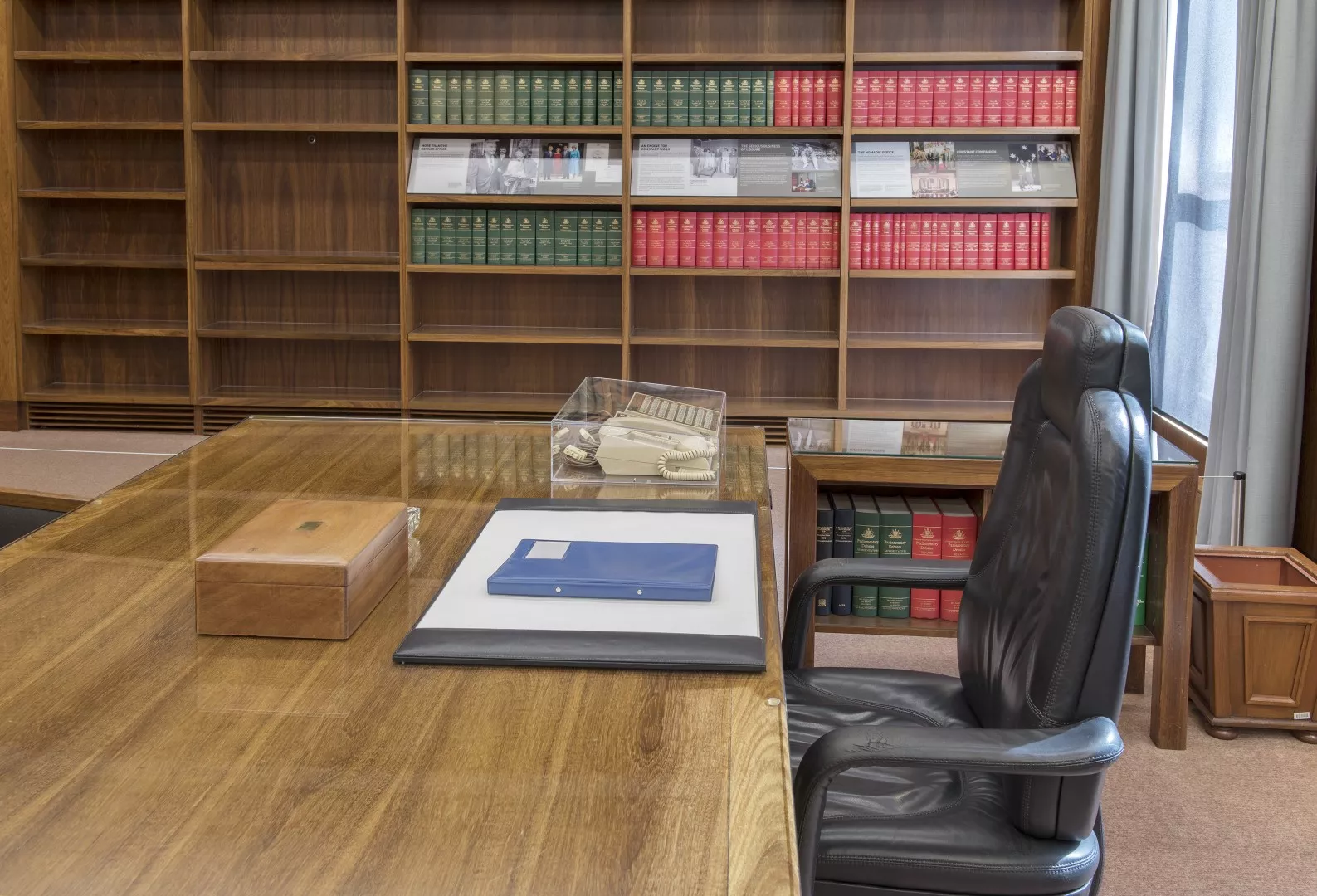 The honey-coloured black bean timber top of the prime minister's desk with a leather chair next to it. On the desktop there is a black leather blotter and a 1980s Telecom Commander telephone.