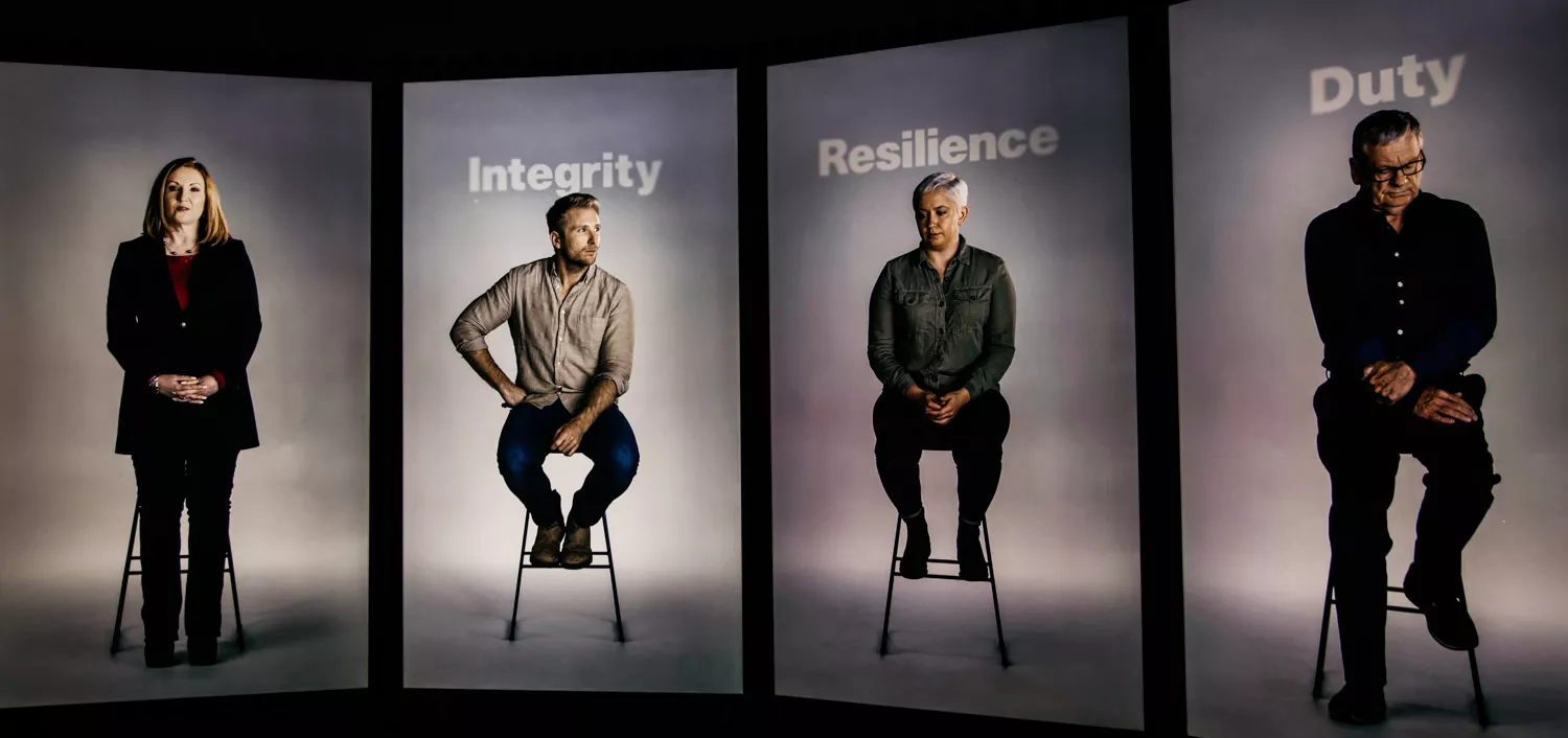 Four video screens with a person sitting on a stool on each screen. The words integrity, resilience and duty appear above them. Four video screens with a person sitting on a stool on each screen. The words integrity, resilience and duty appear above them.
