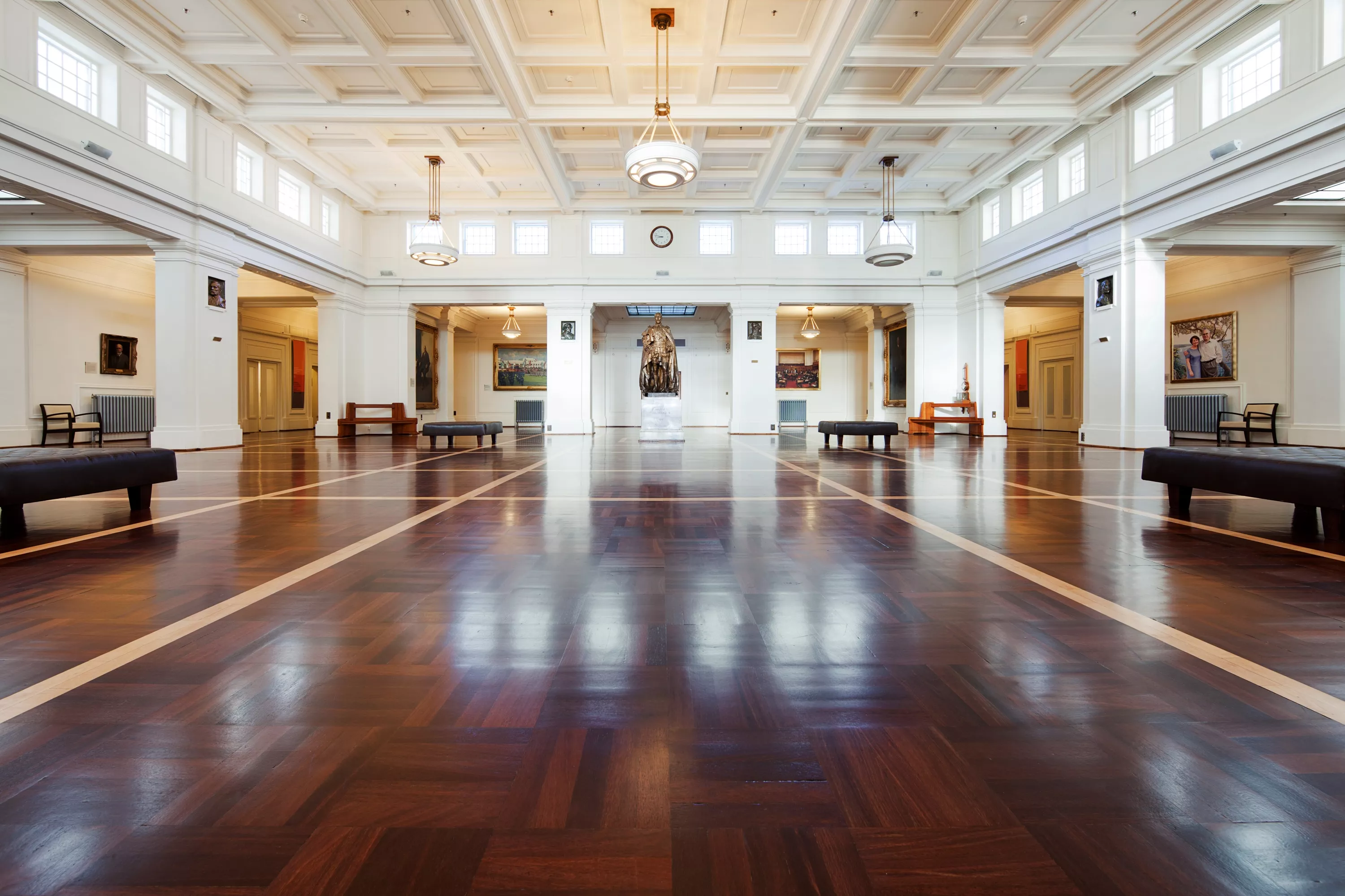 The large central room of Old Parliament House, King's Hall, features timber floors, white ornate ceilings and a statue in the distance. The large central room of Old Parliament House, King's Hall, features timber floors, white ornate ceilings and a statue in the distance.