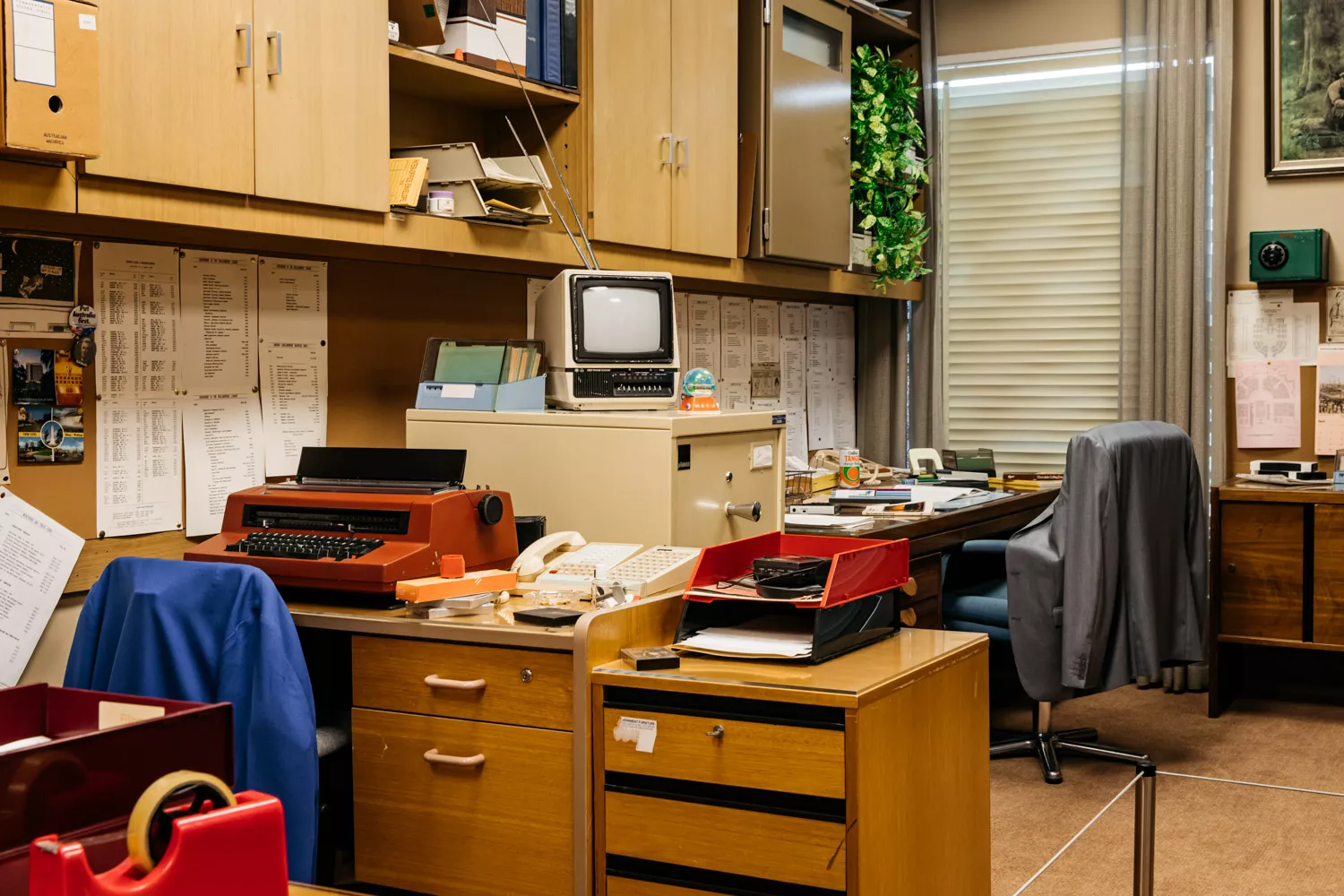 Styled like it's from the '80s, this is the corner of an office typewriters, desks, chairs with jackets over them. Styled like it's from the '80s, this is the corner of an office typewriters, desks, chairs with jackets over them.