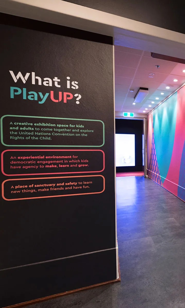 The entrance to PlayUP at MoAD where there are black walls with brightly coloured text and images. The entrance to PlayUP at MoAD where there are black walls with brightly coloured text and images.