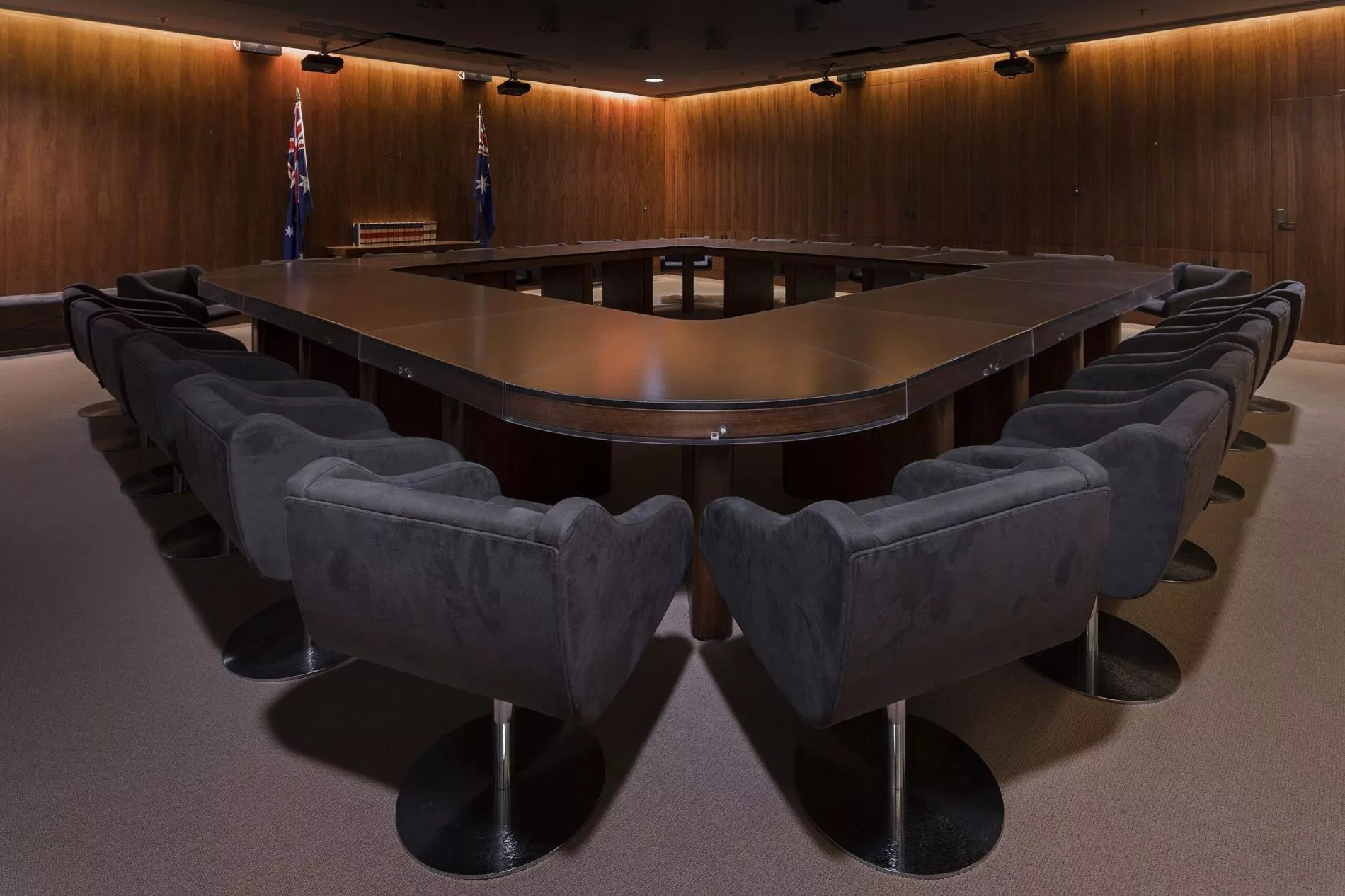 A dark room with heavy curtins and a large, heavy oval shaped table with a hole in the middle surrounded by large grey chairs. A dark room with heavy curtins and a large, heavy oval shaped table with a hole in the middle surrounded by large grey chairs.