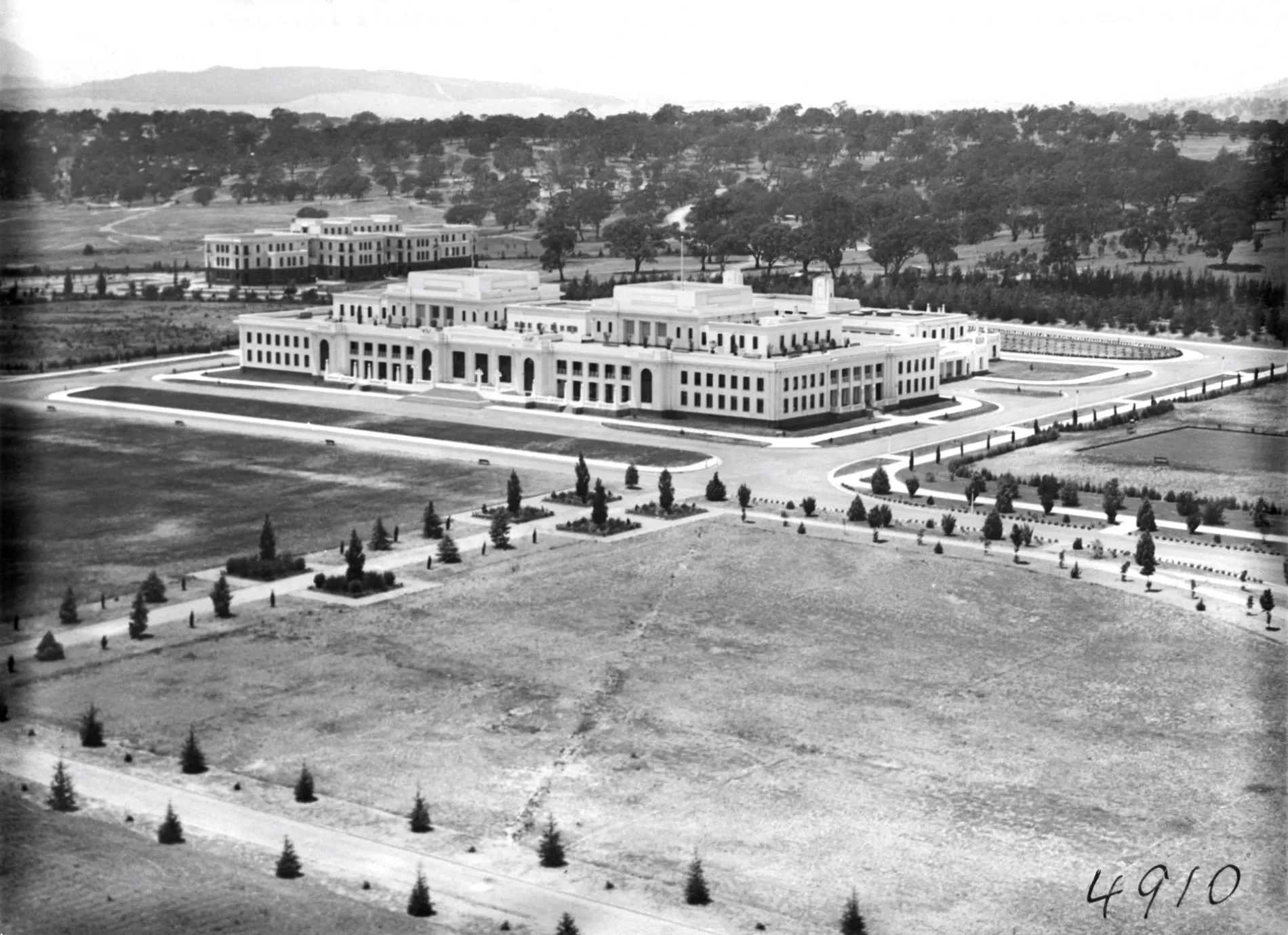 A black and white arial shot of a Old Parliament House, a large white building, surrounded by newly cleared land with planted trees. A black and white arial shot of a Old Parliament House, a large white building, surrounded by newly cleared land with planted trees.